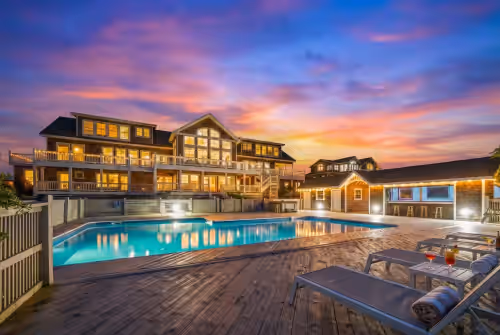 Spacious pool deck with lounge chairs and cocktails set against a colorful sunset. at Oceanfront Estate|18BR, Sleeps 40